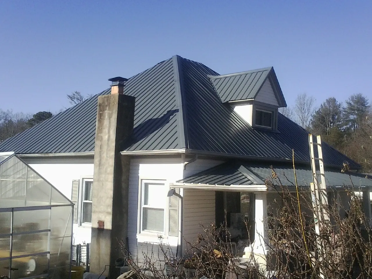Dark blue standing seam metal roof on a white farmhouse with dormer — Slate & Tile Roof Repair by Roofing Brothers in Bozeman