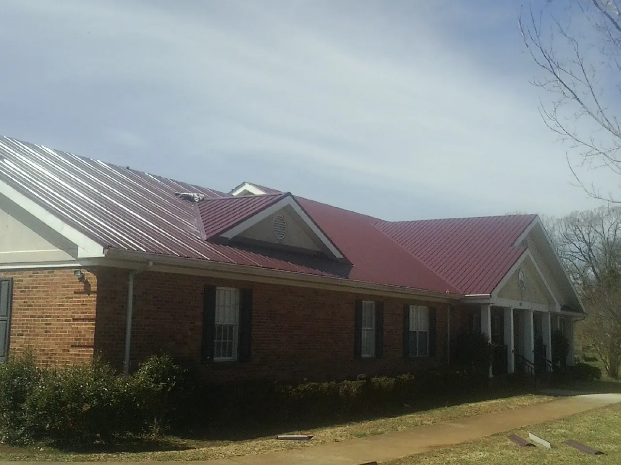 Red metal roof with gabled entries on a long brick building, from a Hail Damage Roof Repair job in Bozeman