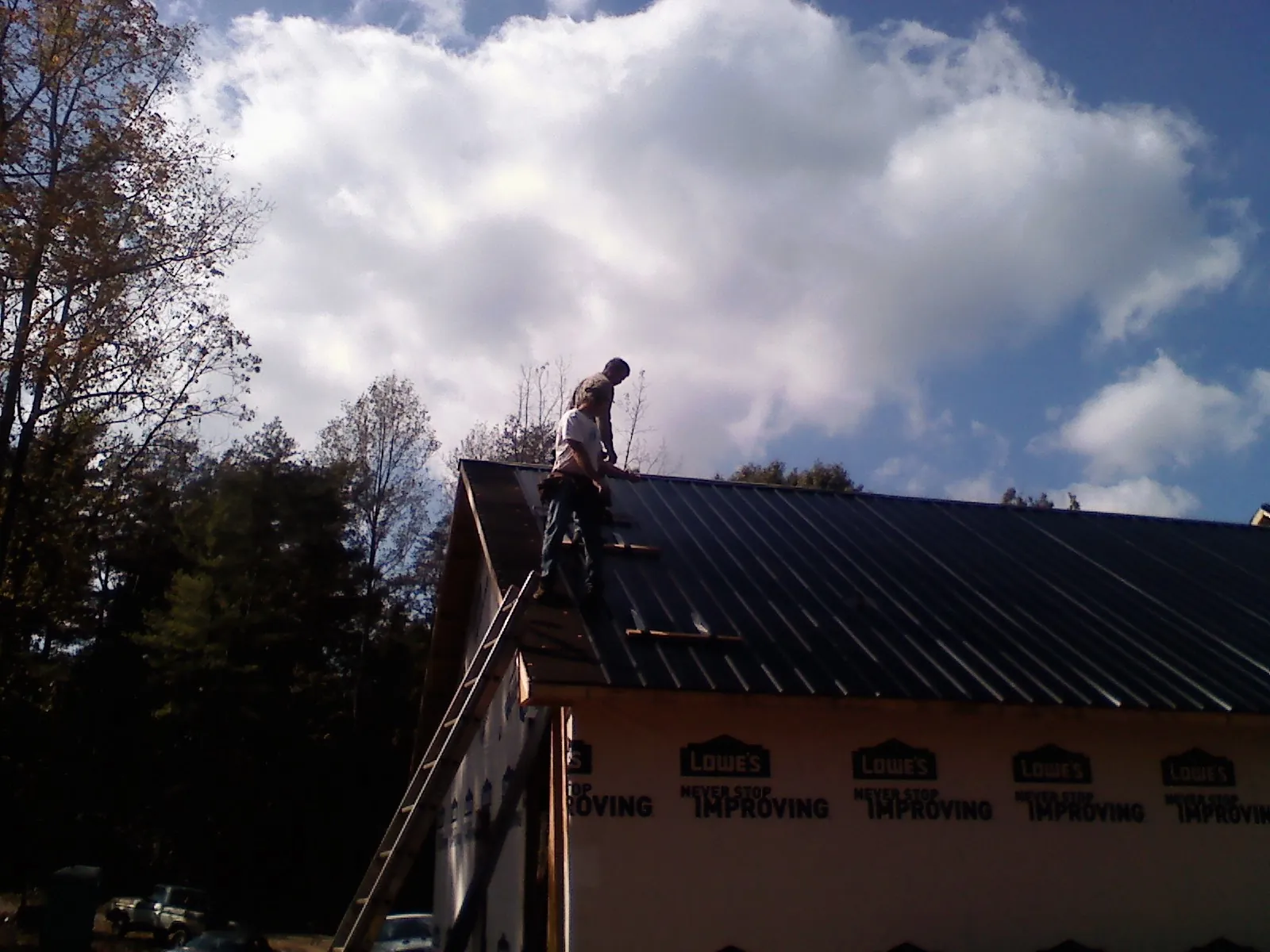 Roofer fastening dark metal panels high against a cloudy sky, from a Roof Inspection job in Bozeman