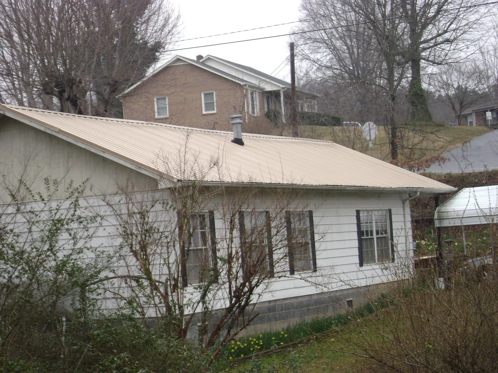 Tan metal roof on a white sided house set into a hillside — Commercial Roofing by Roofing Brothers in Bozeman
